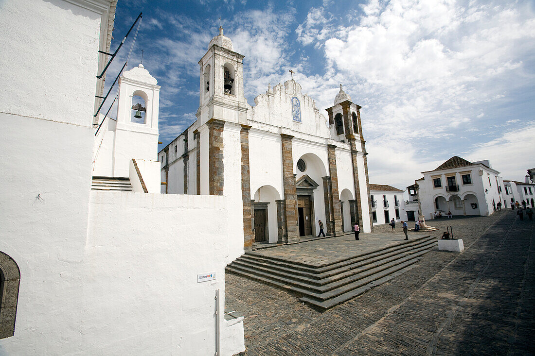 Die befestigte Kirche von Monsaraz steht prominent im Dorf, umgeben von historischer Architektur vor blauem Himmel