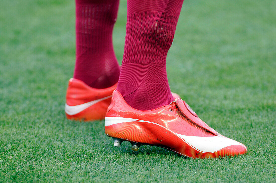 Close up view of vibrant red soccer cleats worn on a lush green field, highlighting sports and athleticism.