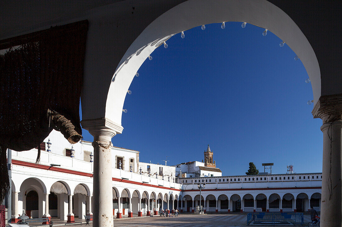 Besuchen Sie den lebhaften Markt in Carmona, wo weiß getünchte Mauern und Torbögen eine beeindruckende architektonische Landschaft unter einem klaren blauen Himmel bilden