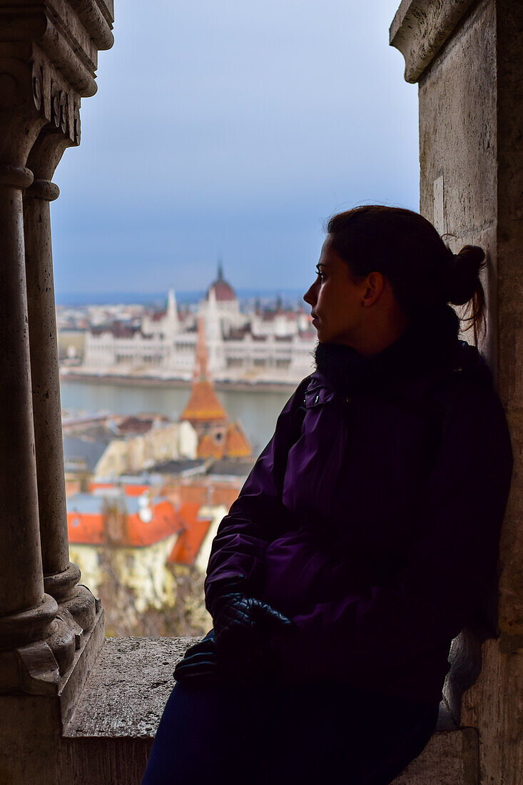 Young woman enjoying the view of Parliament building, Chain Bridge and Danube River through old columns, Budapest, Hungary, Europe