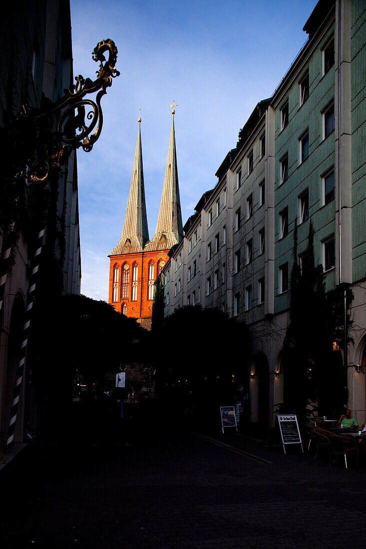 The historic Nikolaikirche stands prominently at the end of a serene street in Berlin, illuminated by the fading evening light.