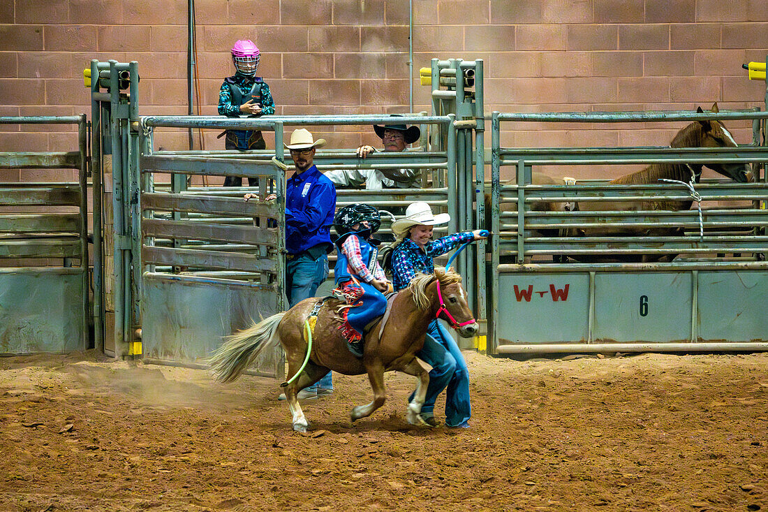 A young cowboy rides a small bucking pony with some help from his mother at the Moab Junior Rodeo in Moab, Utah.