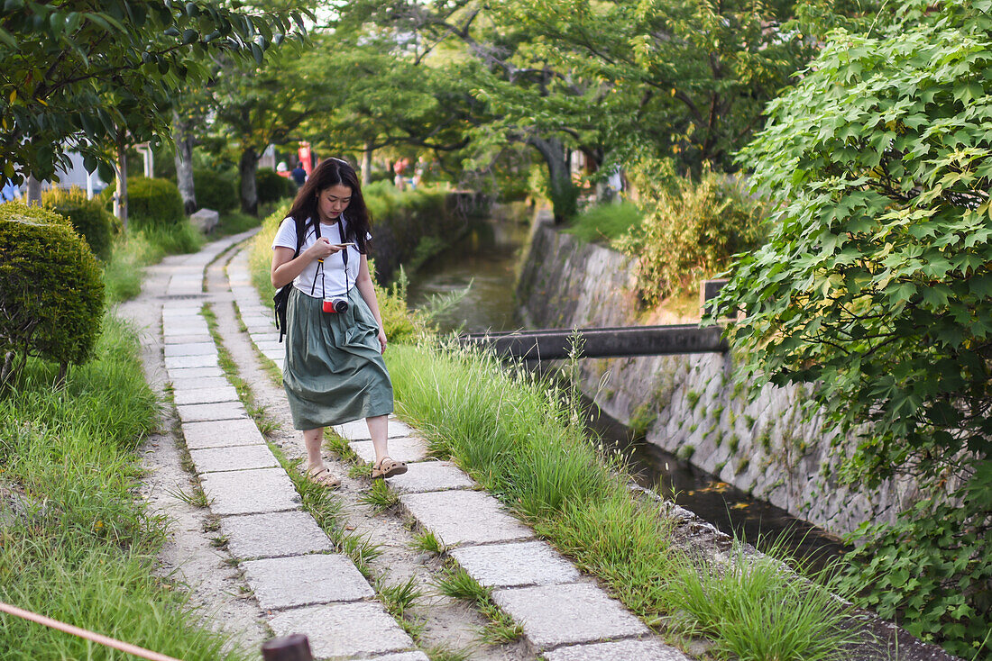 Junge Frau mit Smartphone im Philosopher's Walk in Kyoto, Japan