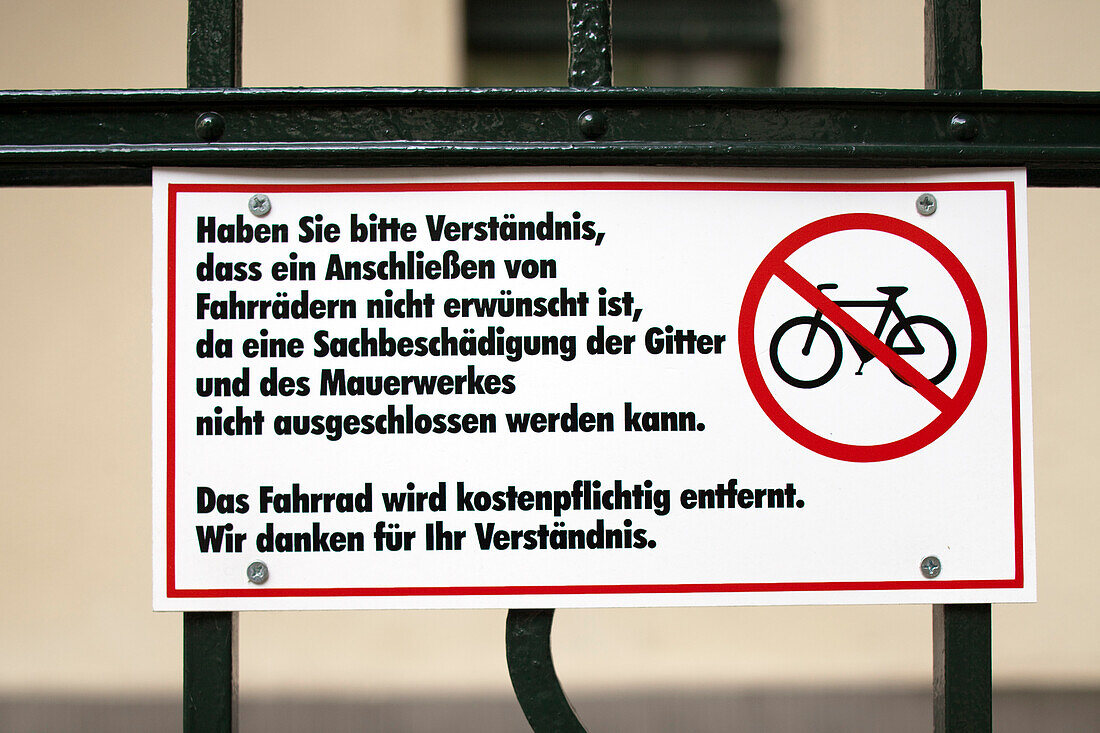 A sign in Berlin instructs against locking bicycles, warning of potential damage to gates and walls, reflecting local regulations.