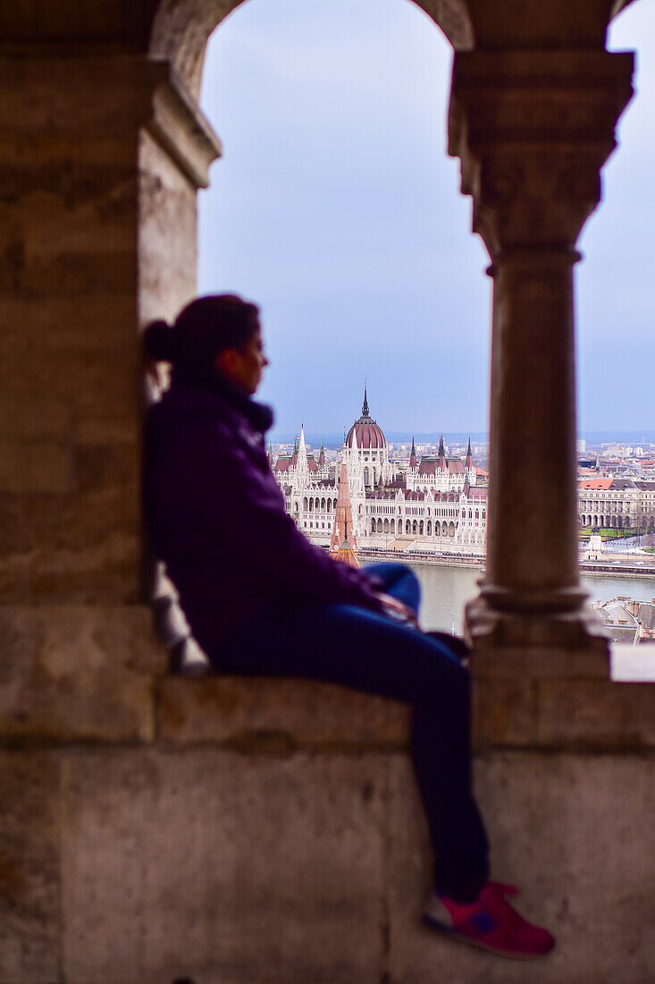 Young woman enjoying the view of Parliament building, Chain Bridge and Danube River through old columns, Budapest, Hungary, Europe