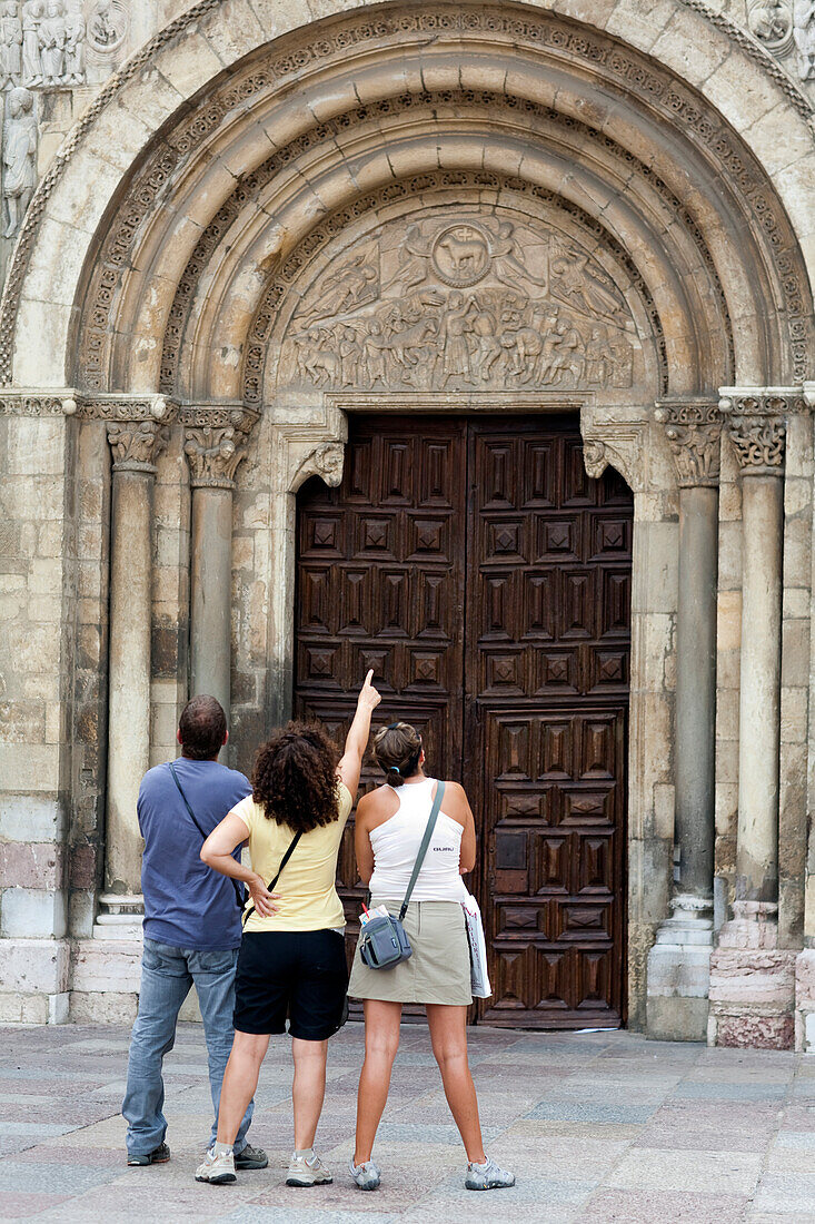 Three visitors appreciate the intricate details of the Romanesque entrance to San Isidoro Basilica in León, Spain.