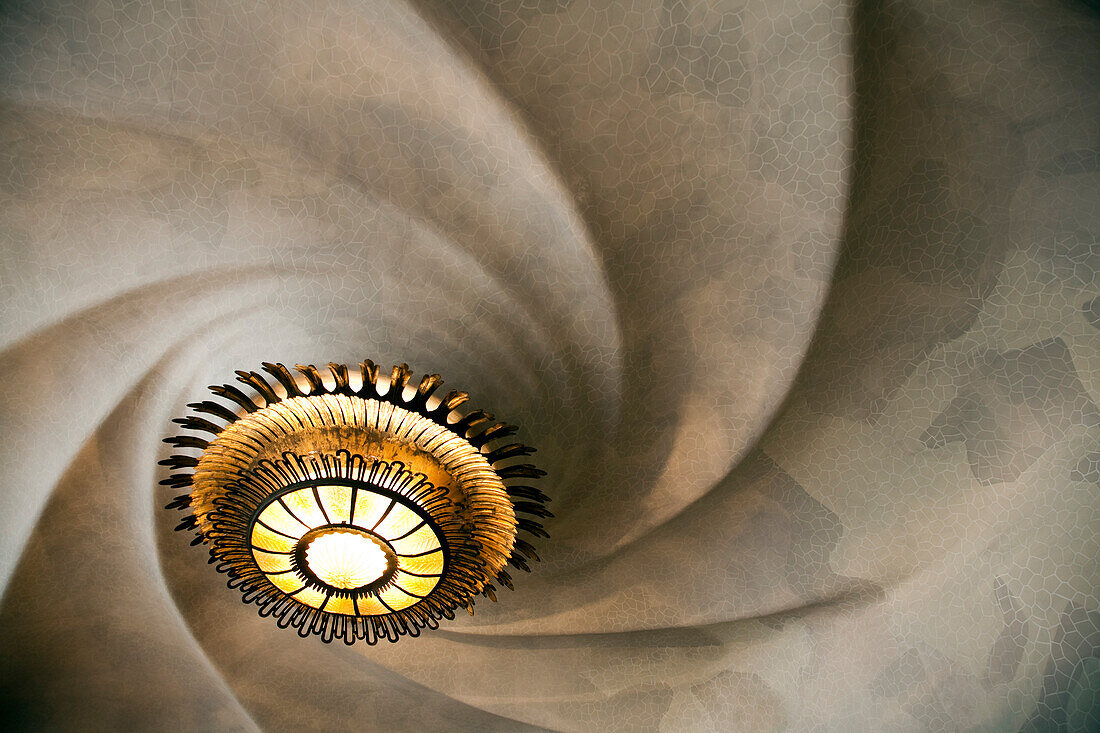 Barcelona, Spain, Sept 4 2008, Gaze at the swirling ceiling pattern adorned with an ornate chandelier, showcasing Gaudí’s architectural brilliance in Barcelona.