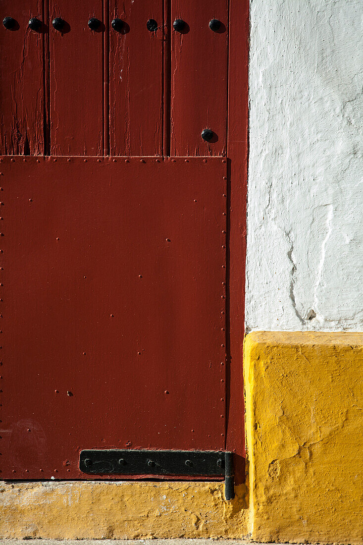 A close-up look at the rustic red door of the Maestranza bullring in Seville, showcasing its historic charm and architectural details.