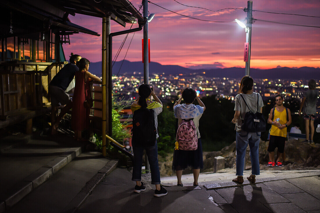 Menschen genießen den nächtlichen Blick auf Kyoto vom Aussichtspunkt des Fushimi Inari Taisha-Tempels, Kyoto, Japan