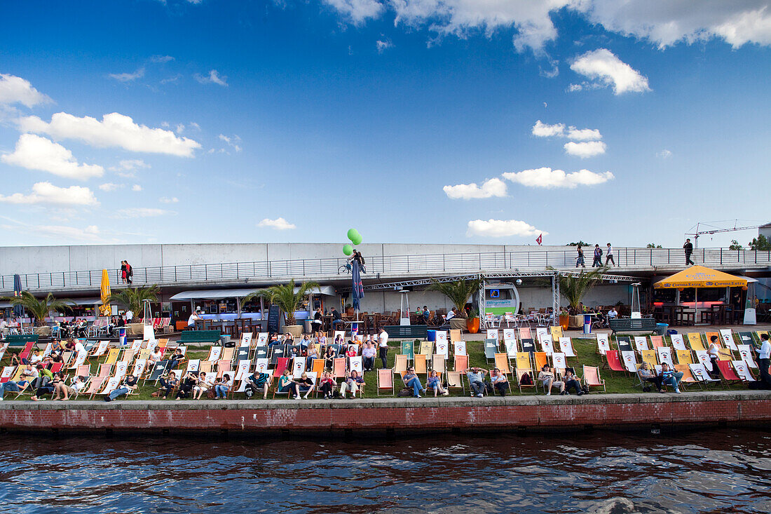 Besucher genießen ihre Freizeit in einer Open-Air-Bar an der Spree, umgeben von Liegestühlen und einer lebhaften Atmosphäre in Berlin