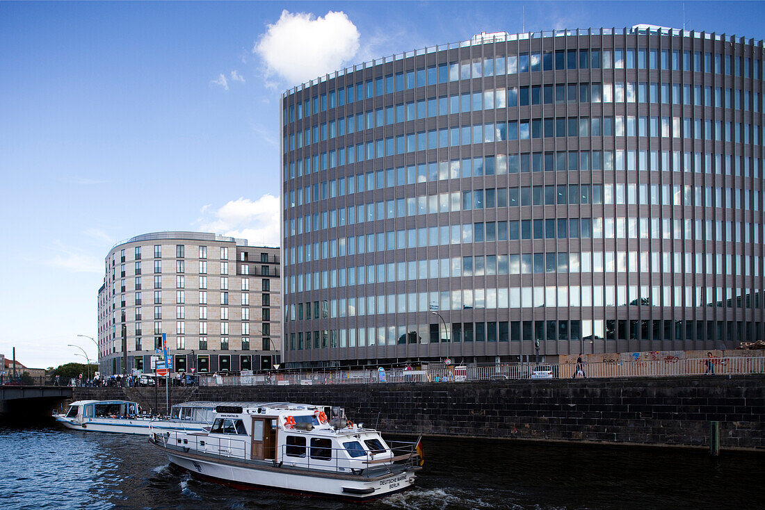 Contemporary buildings rise on the south bank of the Spree river with boats passing by, showcasing Berlin\'s vibrant urban landscape.