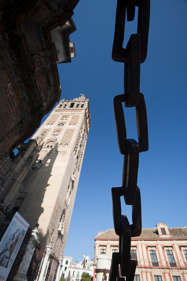 La Giralda tower framed by chains and the blue sky above the Cathedral of Sevilla.