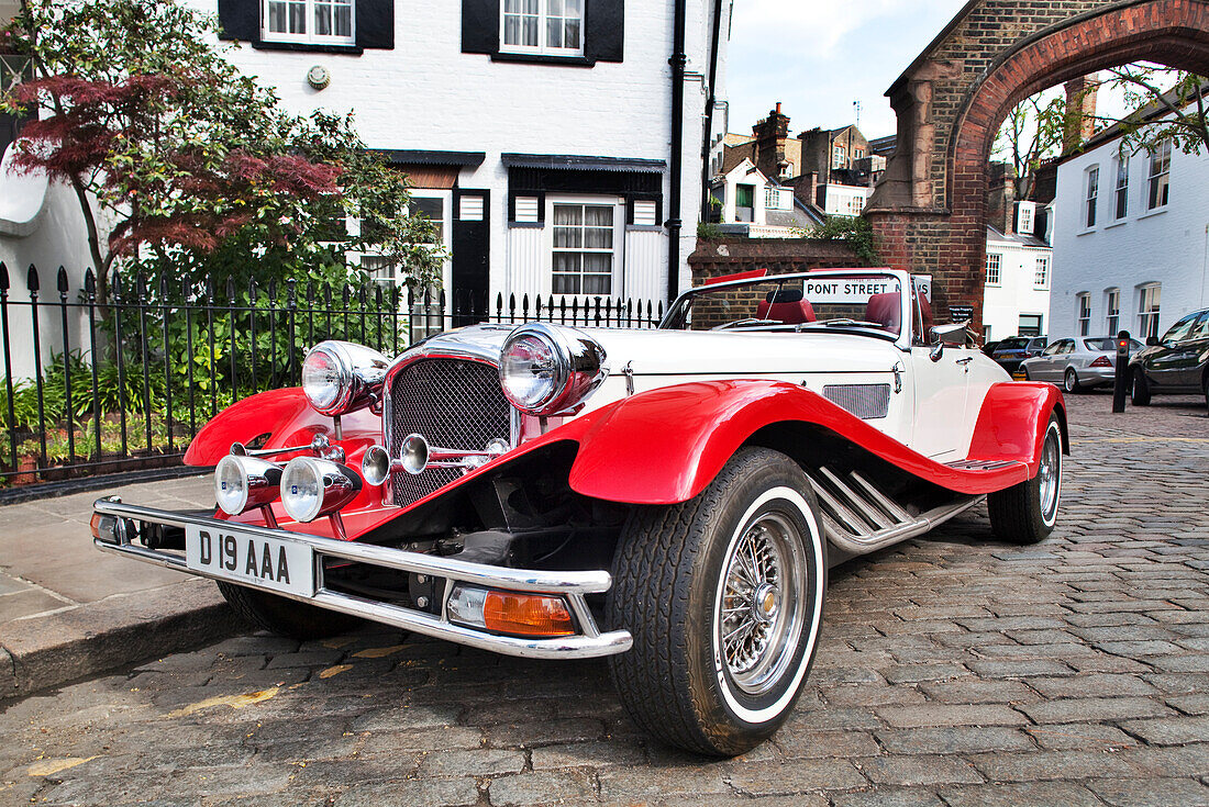 A classic vintage car stands gracefully along Pont Street in the Kensington area of London, surrounded by quaint buildings.