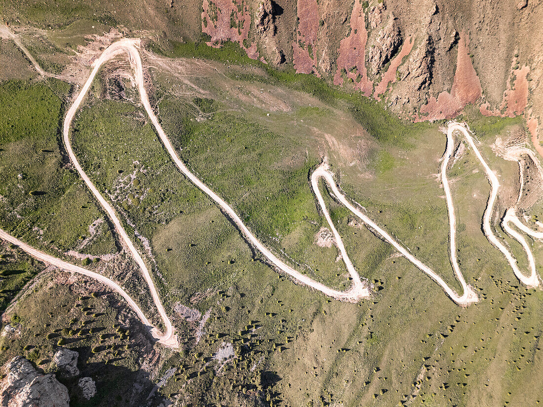 Aerial view of a winding mountain road curves, Kalmak Ashuu Pass, through lush greenery in Kyrgyzstan, Central Asia, Asia