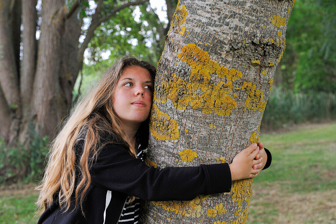 Young girl embracing the trunk of an ash tree, France, Europe