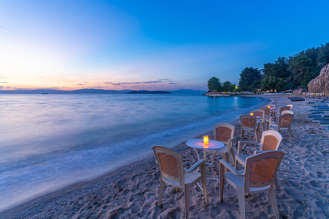 Blick auf Restauranttische am Strand nach Sonnenuntergang, Thassos-Stadt, Thassos, Ägäisches Meer, Griechische Inseln, Griechenland, Europa