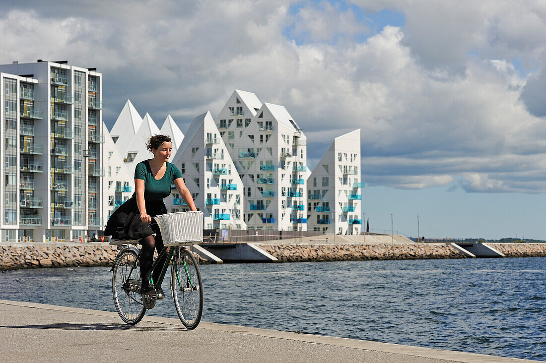 Young woman cycling with The Iceberg apartment building in the background, in the new quarter of Aarhus East constructed by the expansion of the harbour area, Aarhus, Jutland Peninsula, Denmark, Europe