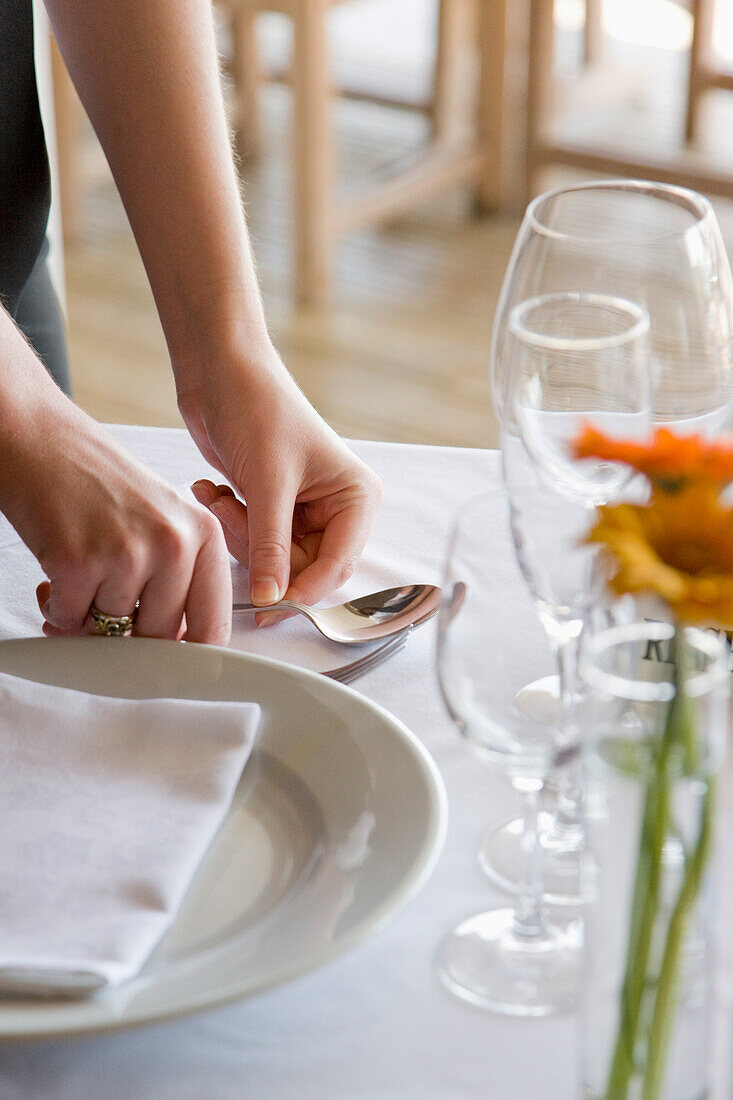 Close up of a waitress's hands arranging cutlery on a restaurant table