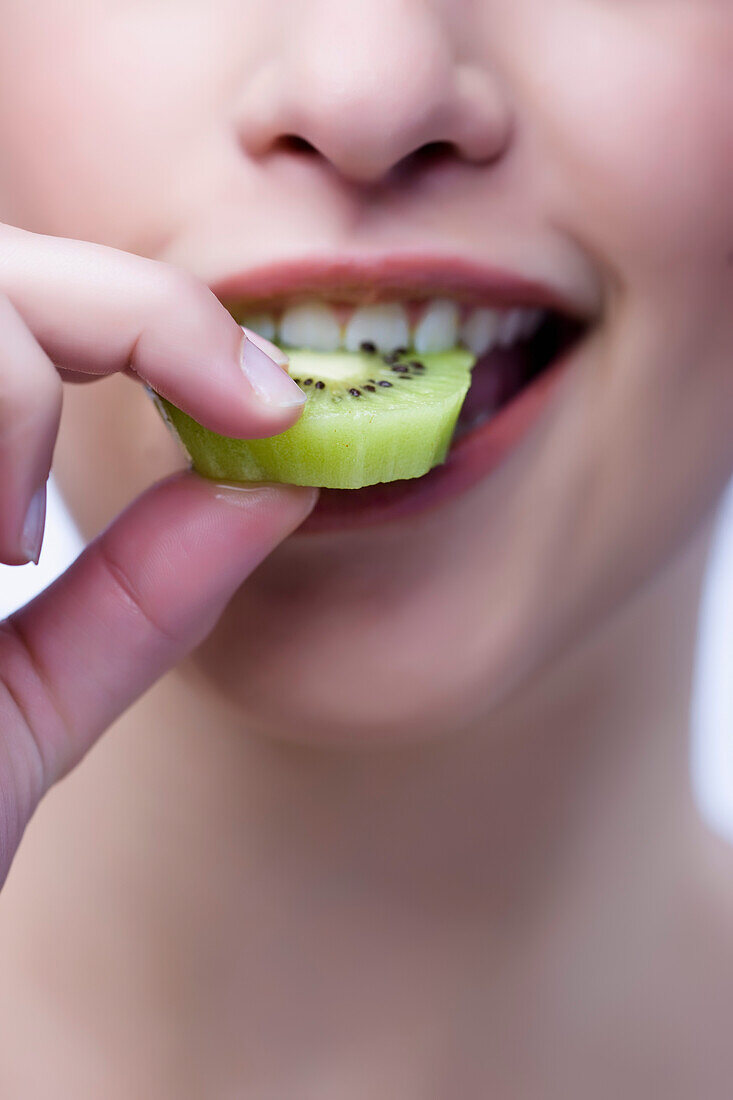 Extreme close up of a woman biting a kiwi slice