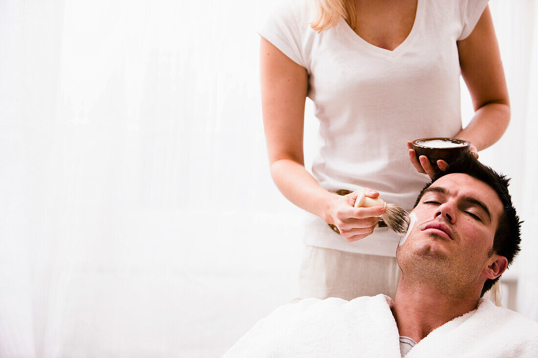 Woman applying shaving cream on man face