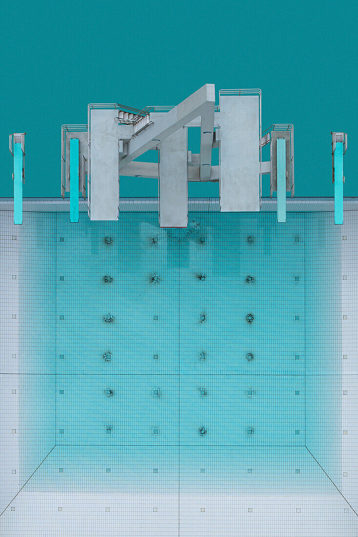 View from above diving platforms and diving boards above half-full blue swimming pool