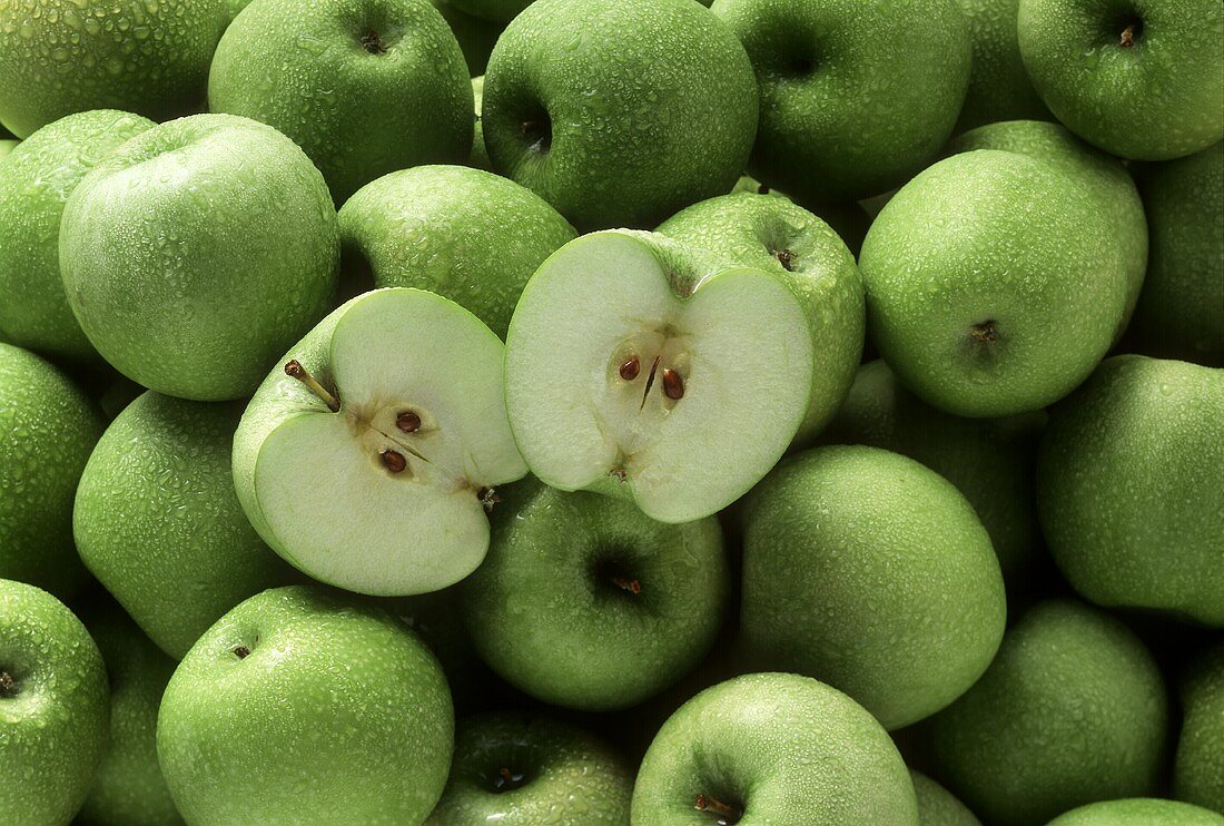 Granny Smith apples with drops of water, one halved