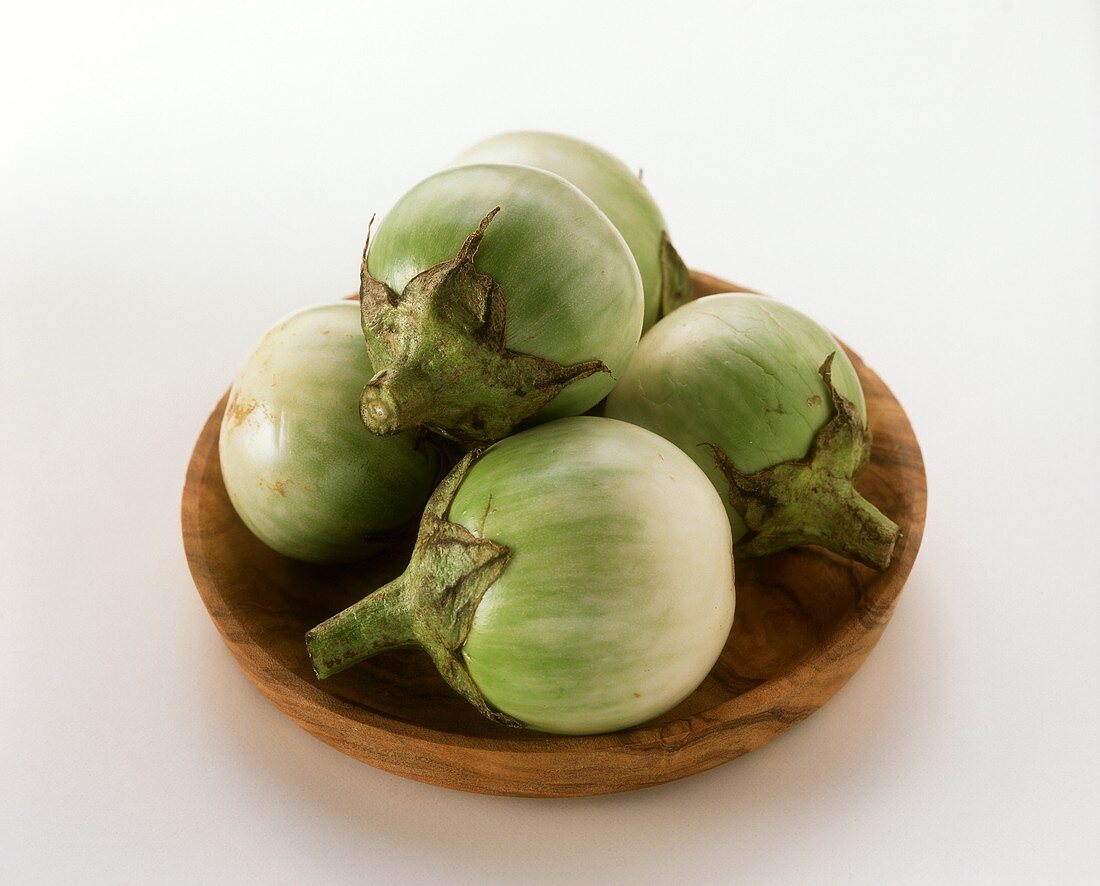 A few green aubergines from Thailand on a wooden plate
