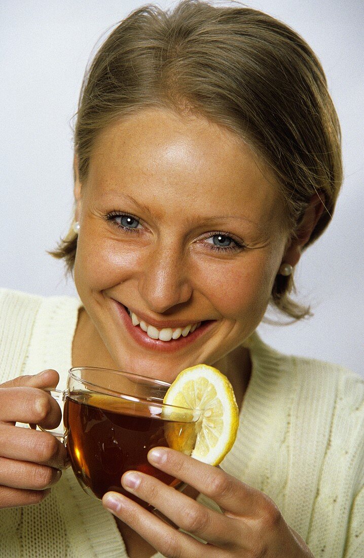 Frau hält eine Tasse Tee, garniert mit Zitronenscheibe