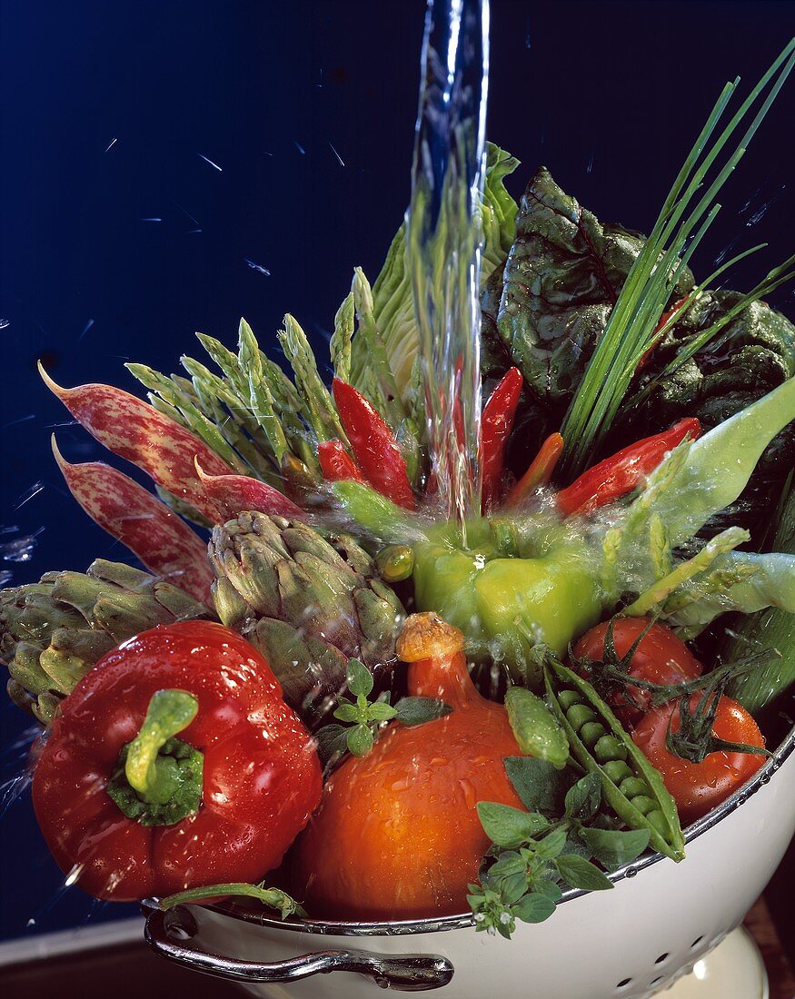 Wasserstrahl trifft auf buntes Gemüse in einer Siebschüssel