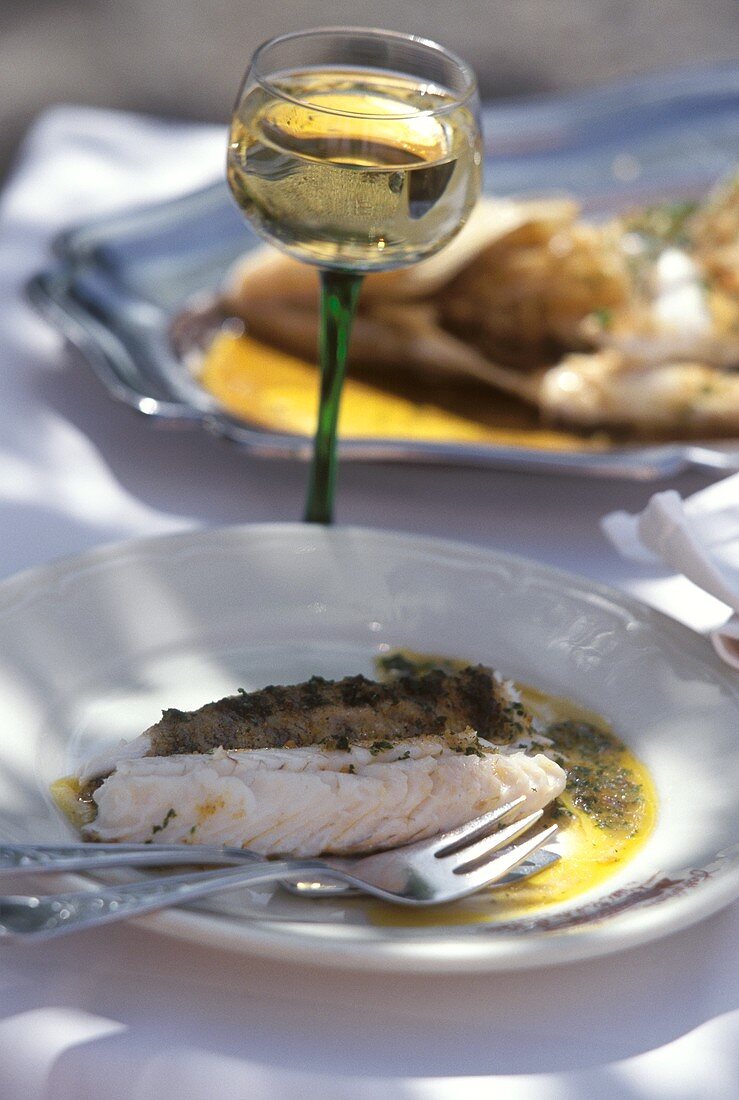 Zander mit Kräutersauce auf Teller und Glas Weißwein