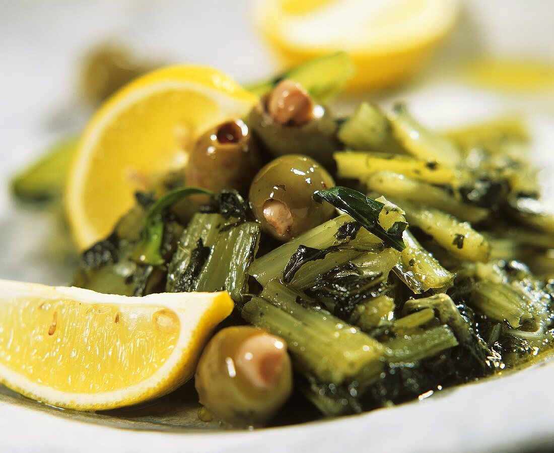 Löwenzahnsalat mit Oliven auf Teller mit Zitronenschnitzen