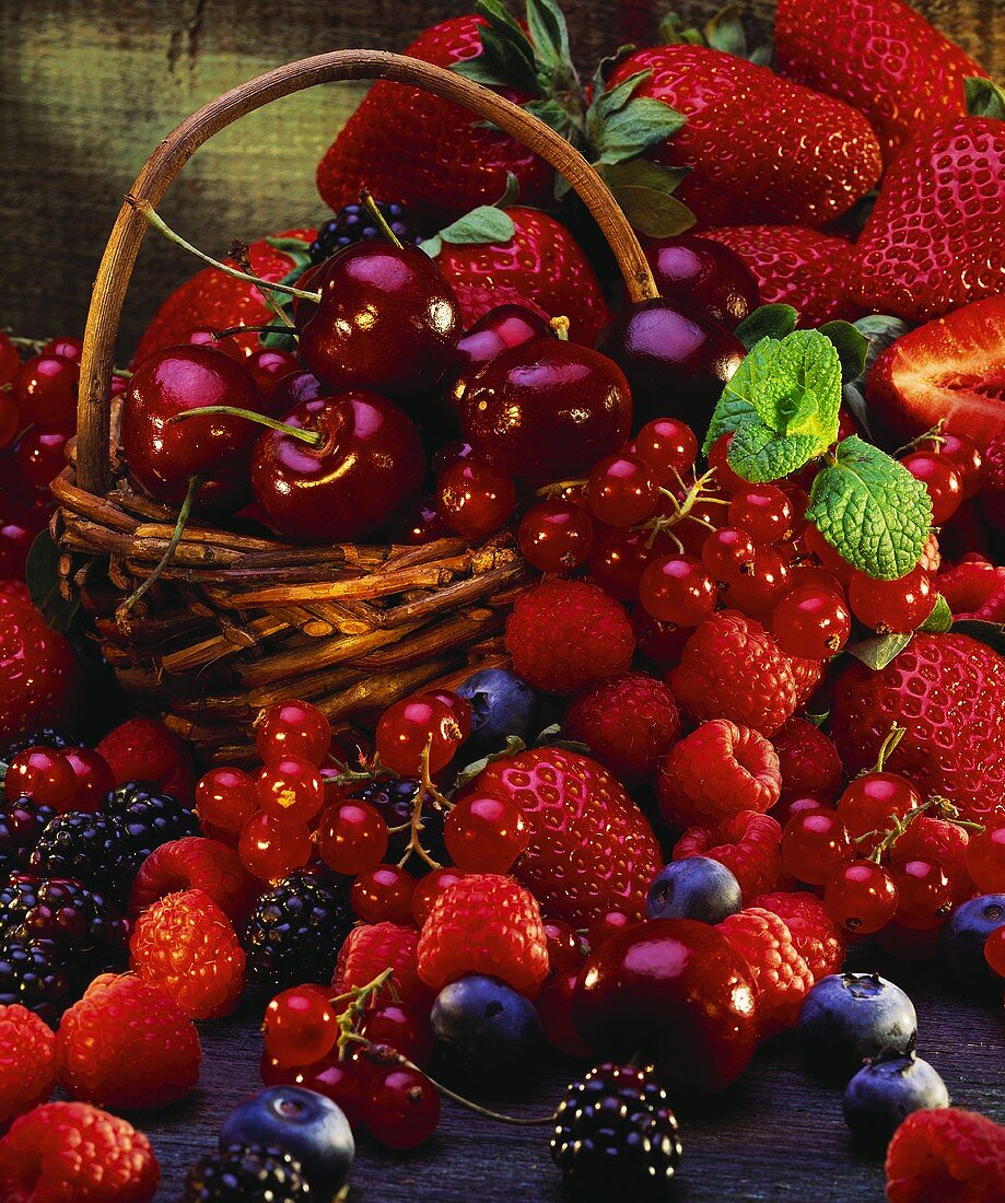 Many different berries and cherries in & around basket