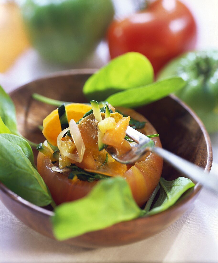 Stuffed tomato with spinach leaves in a wooden bowl