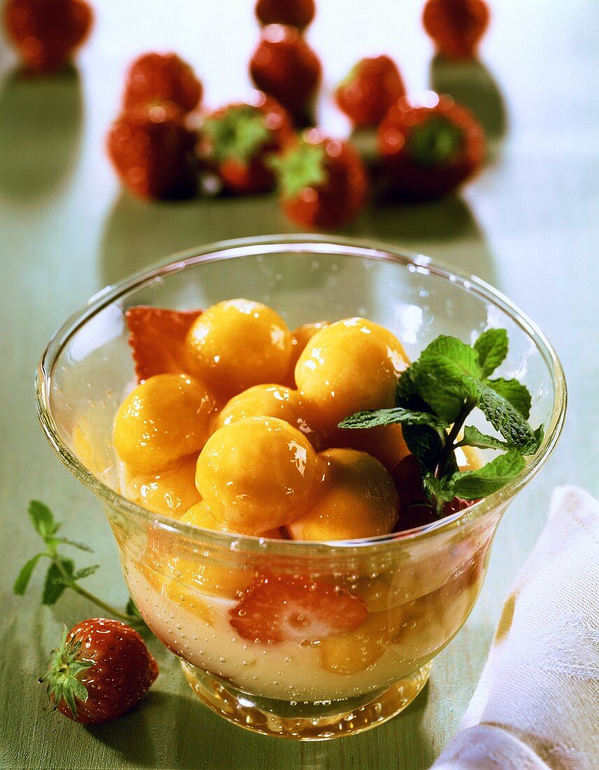 Melon sabayon with strawberries and fresh mint in glass bowl