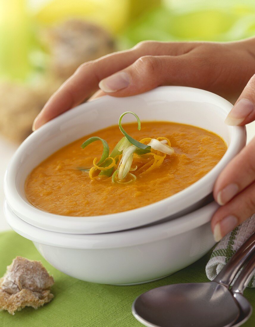 Hands holding a bowl of carrot soup