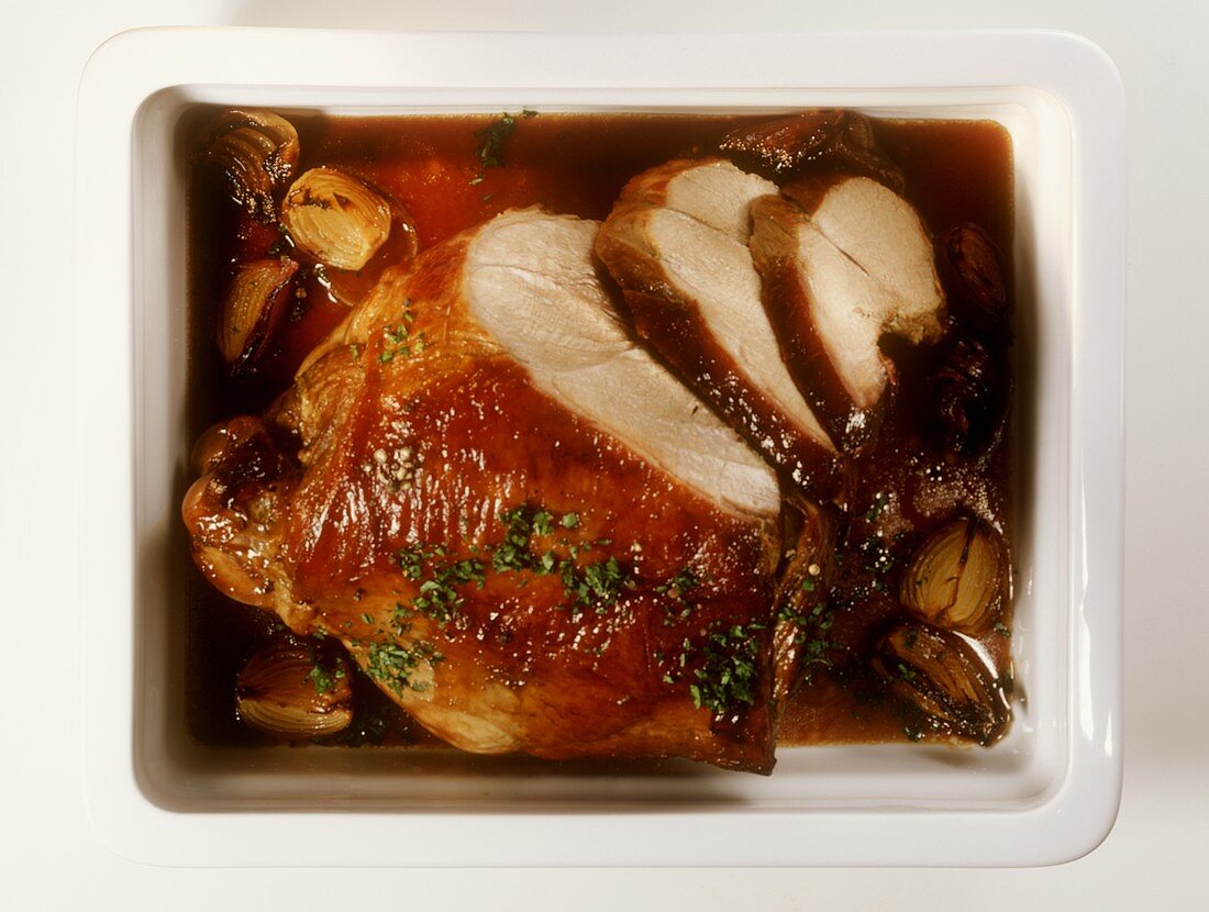 Roast wild boar leg, carved, in glass roasting dish