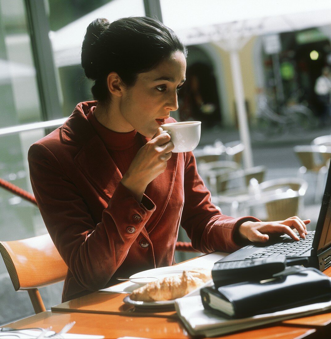 Businesswoman in café using laptop with coffee cup & croissant