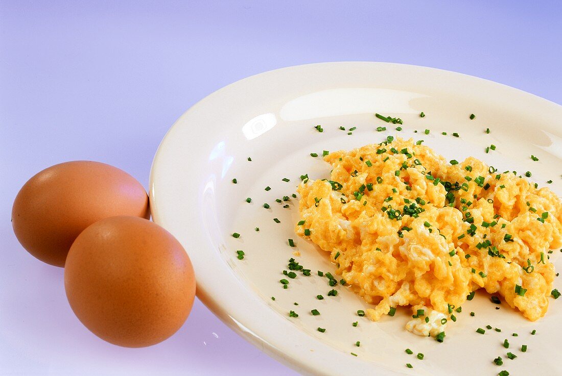 Scrambled egg with snipped chives on plate, two eggs beside it