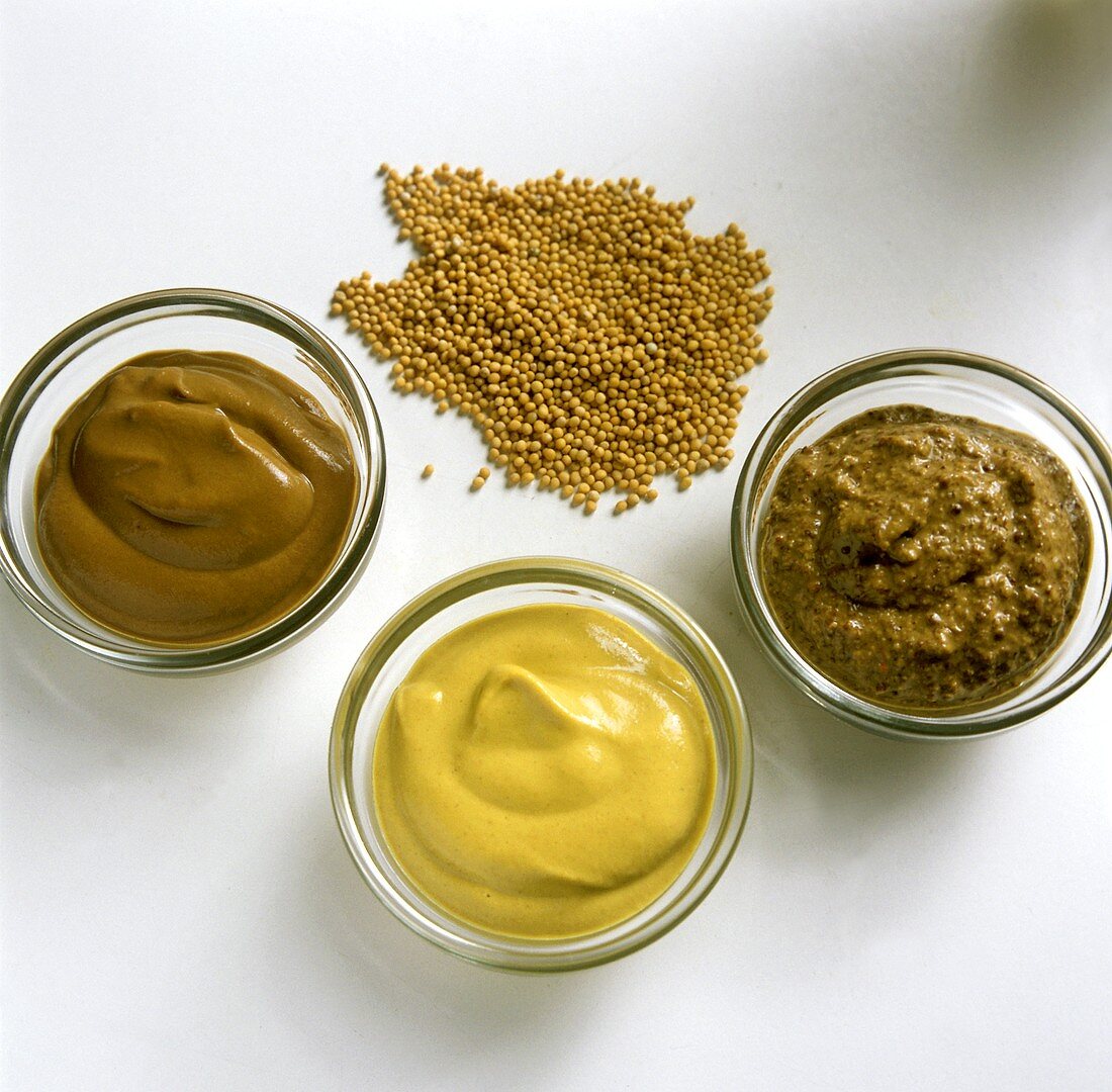 Three different types of mustard in bowls & mustard seeds