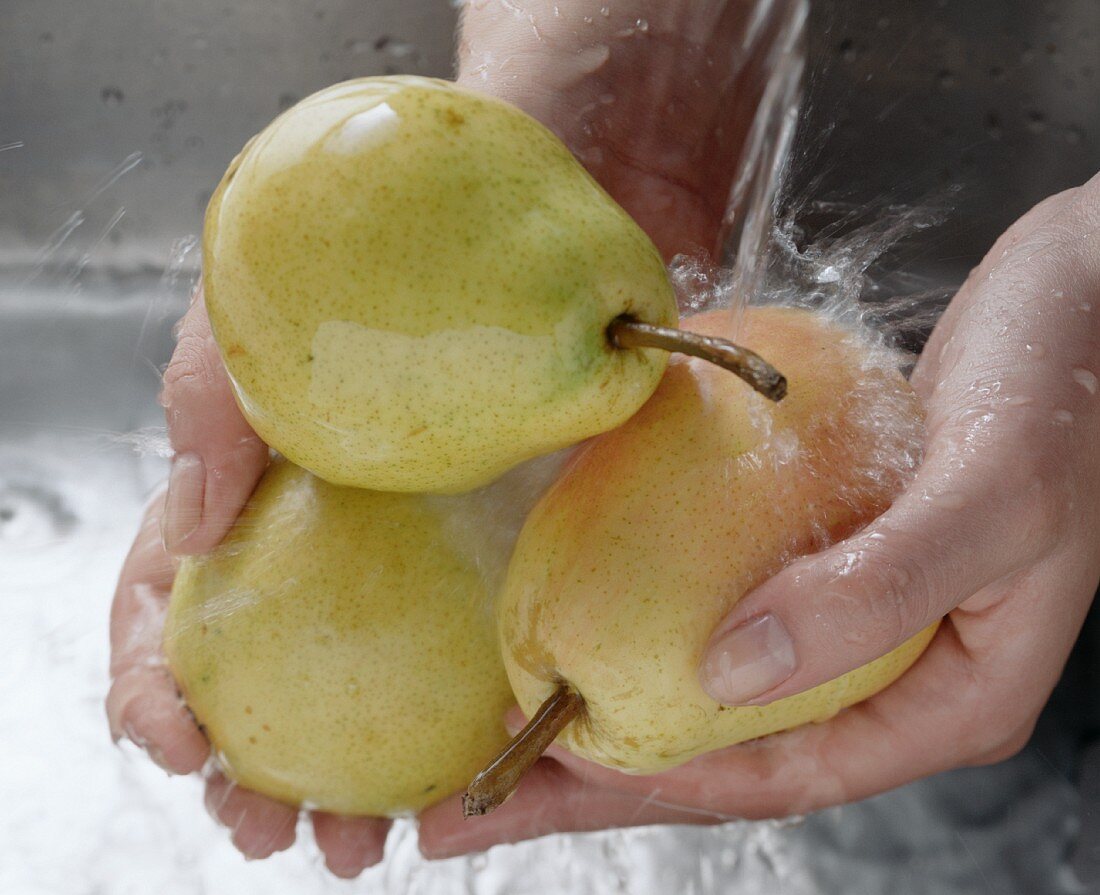 Hands holding three pears under running water