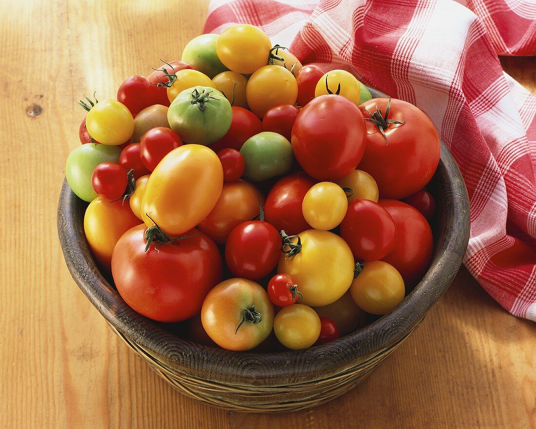 Lots of different tomatoes in wooden dish on wooden platter