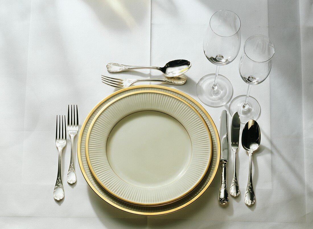 Table setting: gold-rim plates, cutlery, fish cutlery, glasses