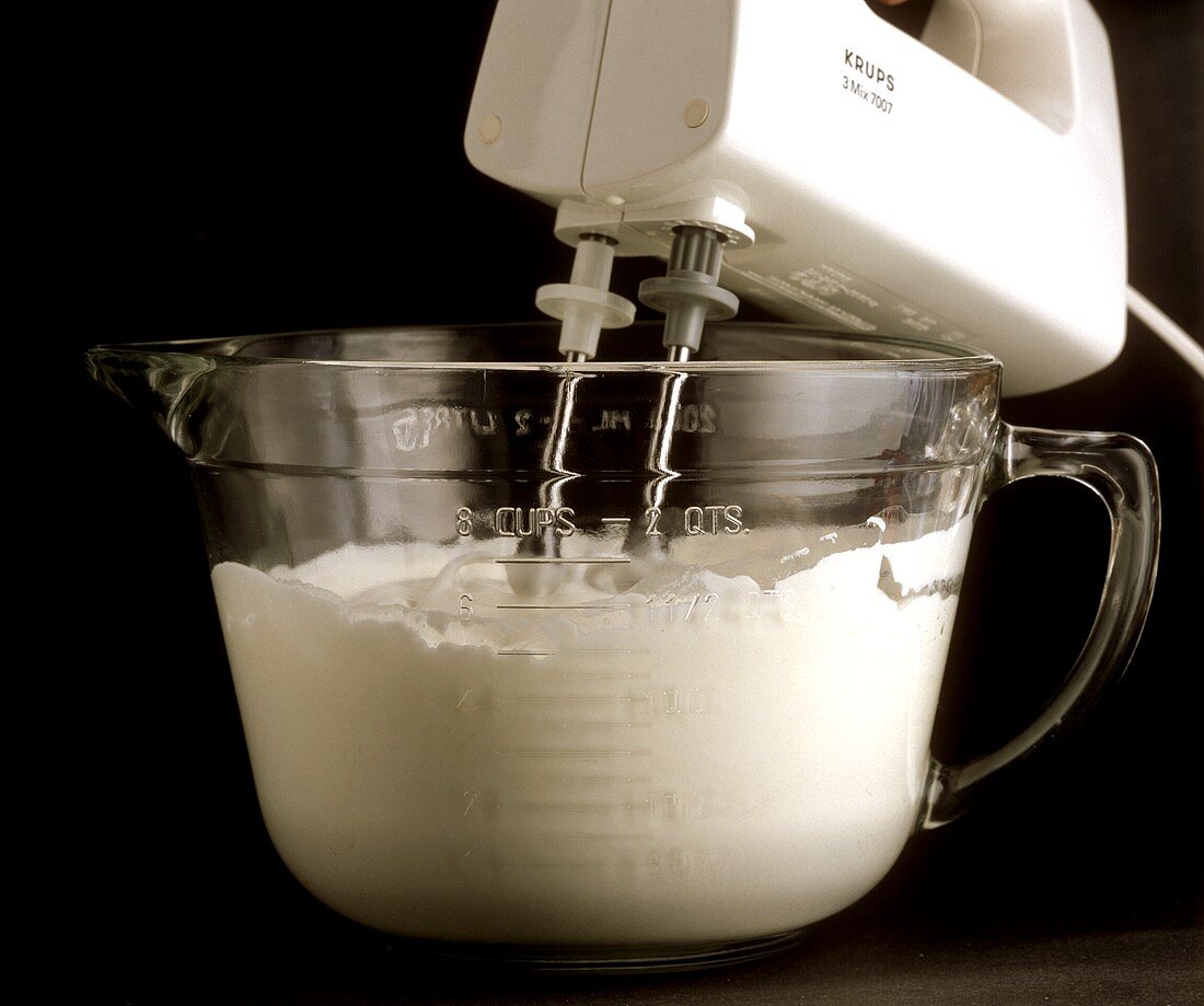 Whipping cream with a mixer against a black backdrop