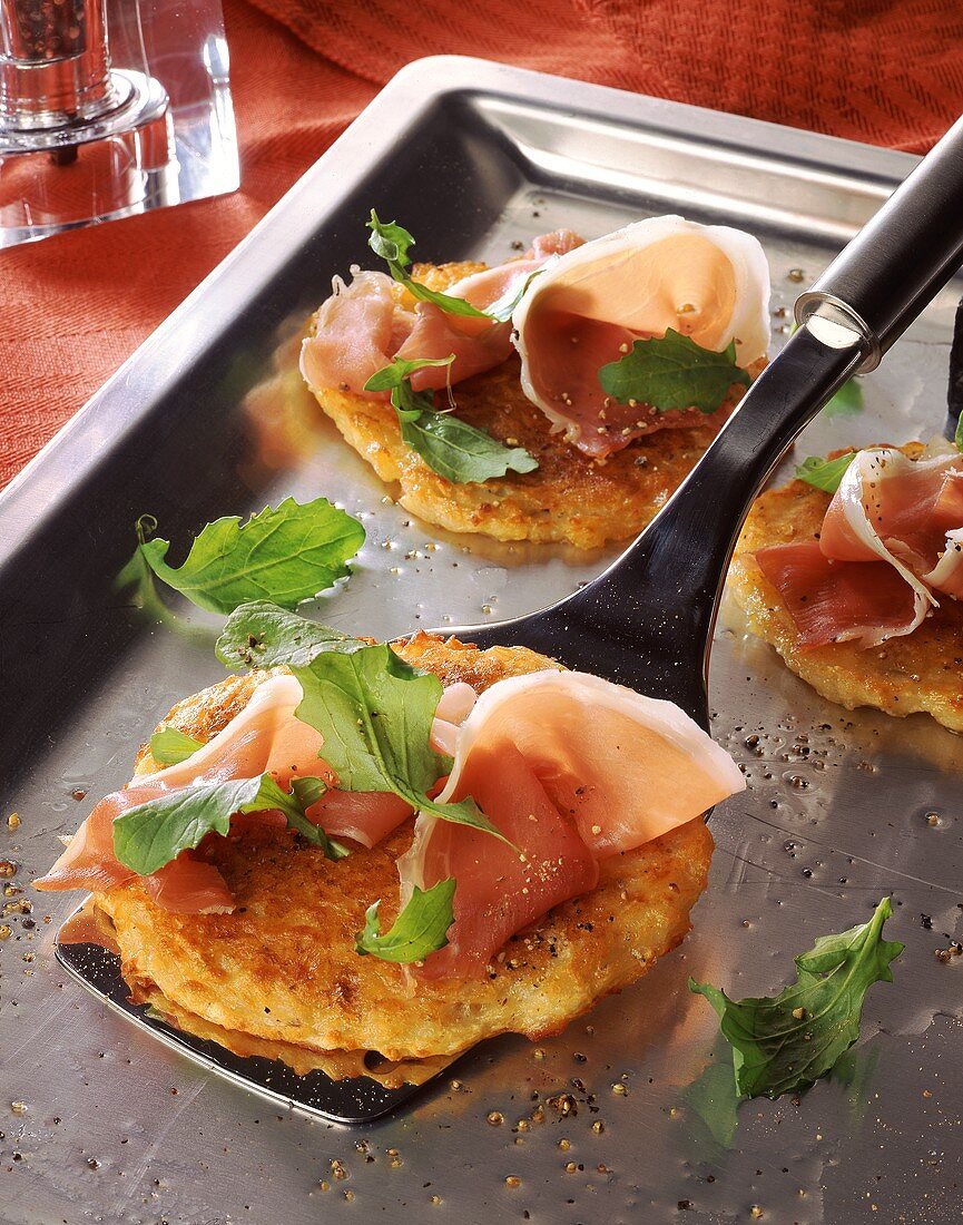 Potato rosti with Parma ham and rocket on baking sheet