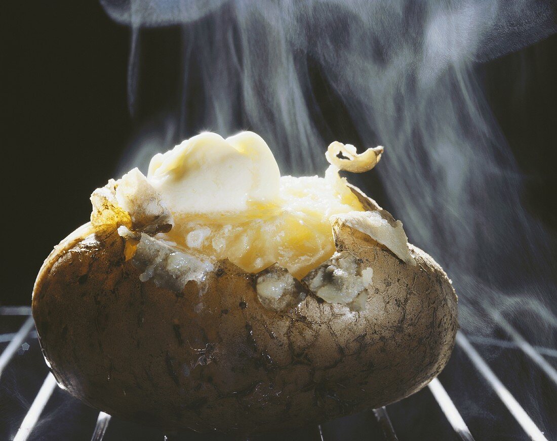 Baked potato with melting butter on oven rack