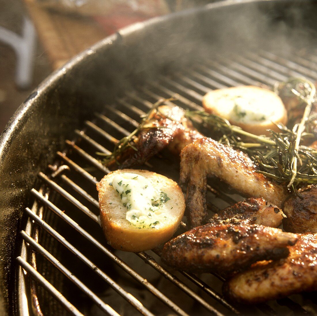 Chicken wings & potatoes on grill rack with sprig of rosemary