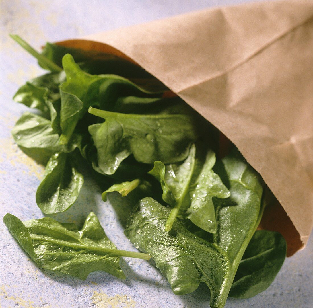 Spinach leaves with drops of water falling out of paper bag