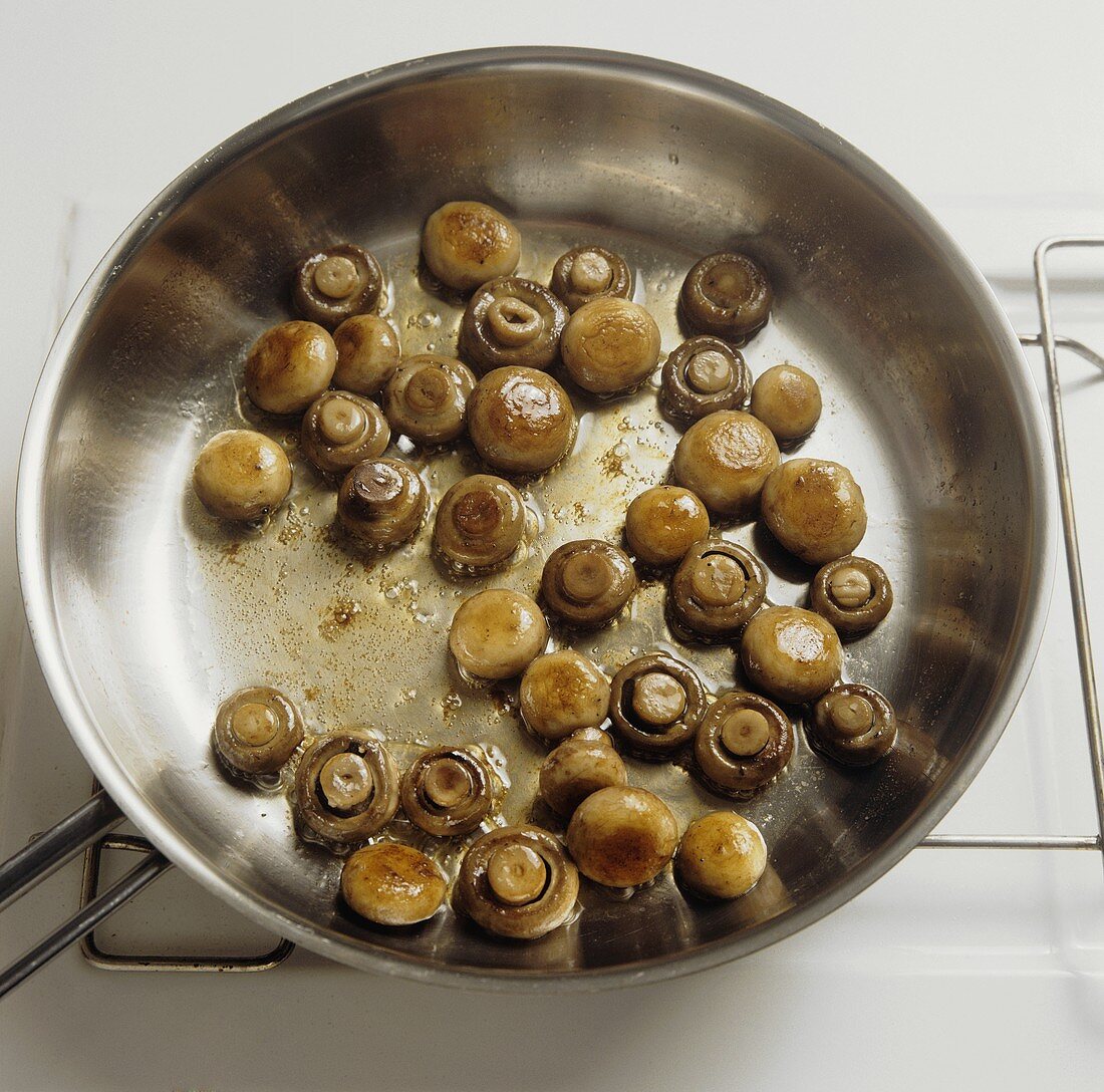Frying button mushrooms and brown mushrooms in a pan