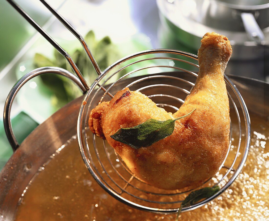 Chicken leg with sage being lifted out of deep-frying fat