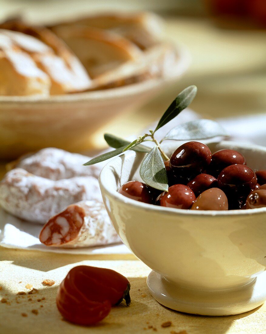 Stillleben mit Oliven in Schale & italienische Salami